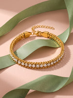 Lundholm Iza schakelarmband met zirkonia goudkleurig langs een saliegroen satijnen lint