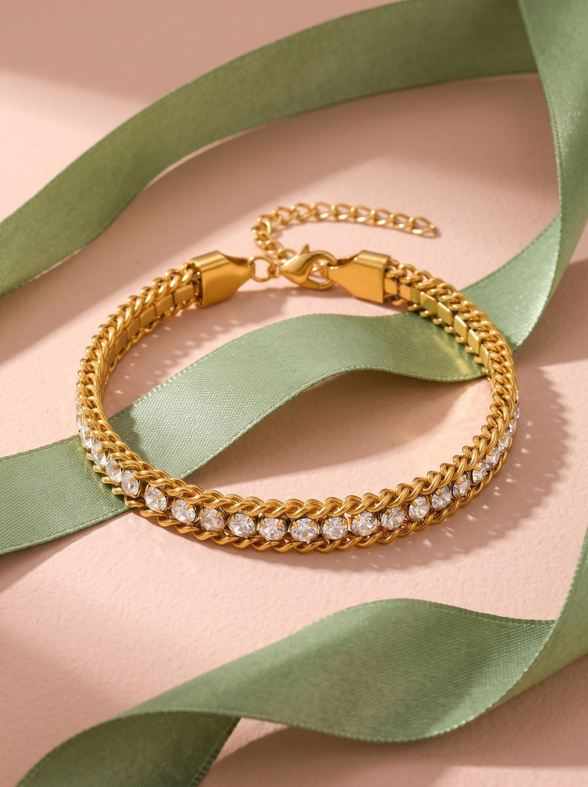 Lundholm Iza schakelarmband met zirkonia goudkleurig langs een saliegroen satijnen lint