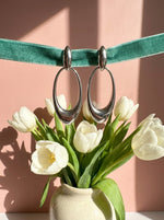 Lundholm Kaia lange ovale oorhangers zilverkleurig aan een fluwelen lint boven witte tulpen