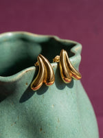 Lundholm Lana sculptural oorknopjes goudkleurig op de rand van een zeegroene keramische vaas
