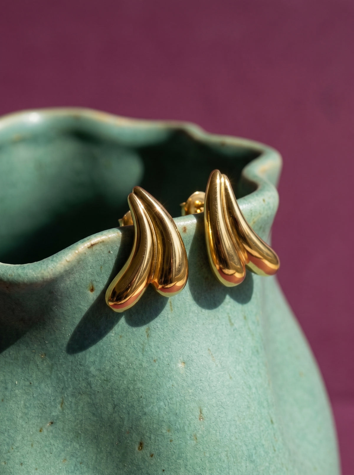 Lundholm Lana sculptural oorknopjes goudkleurig op de rand van een zeegroene keramische vaas