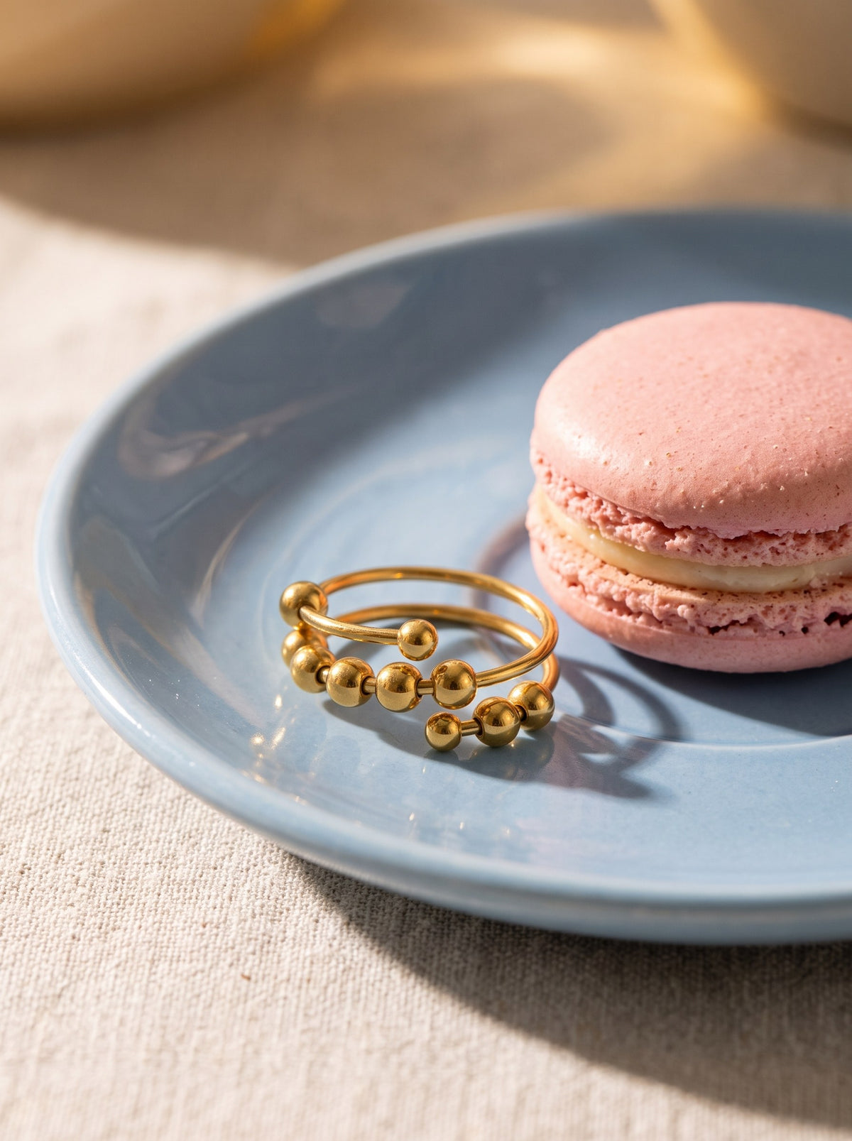 Lundholm Lauren anti-stress ring met bolletjes goudkleurig op een schoteltje met een roze macaron