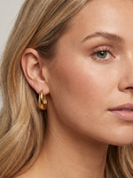 Vrouw draagt Lundholm Lea hoepel oorbellen in goudkleurig stainless steel