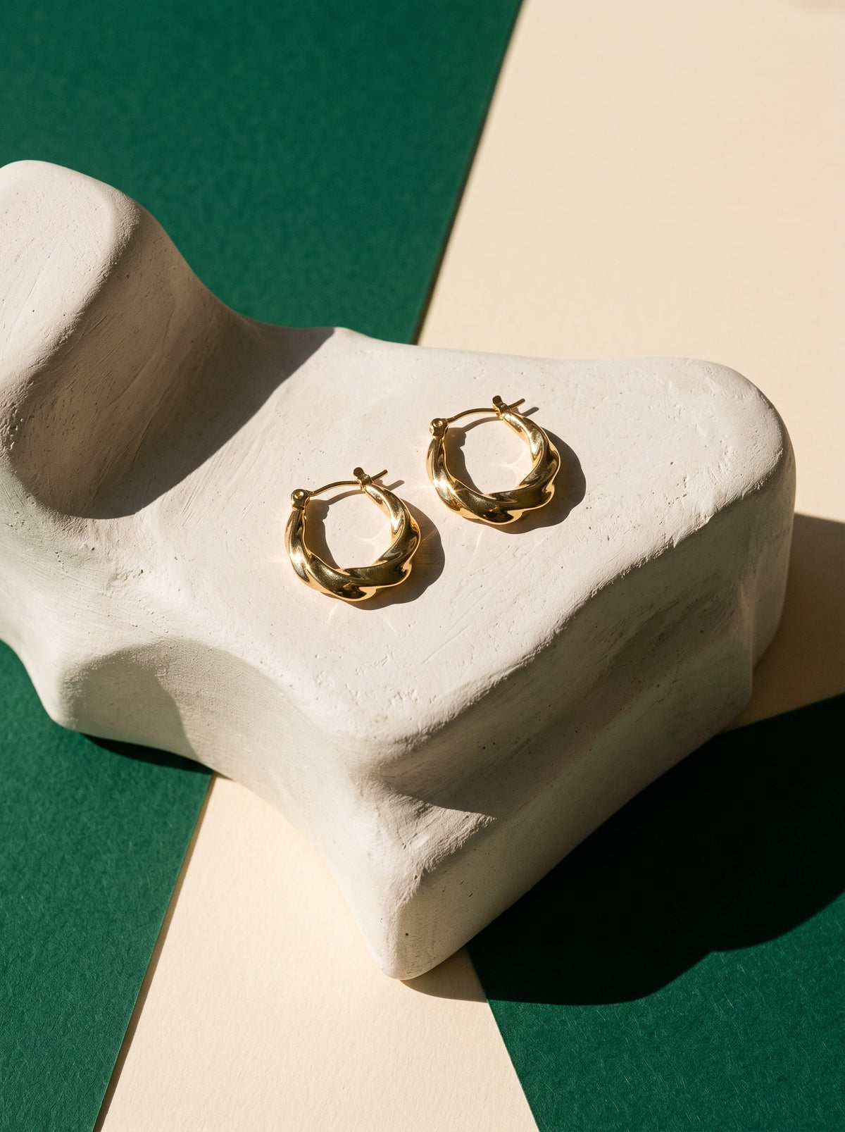 Lundholm Lexi chunky gedraaide oorringen goudkleurig op een witte gipsen sculptuur