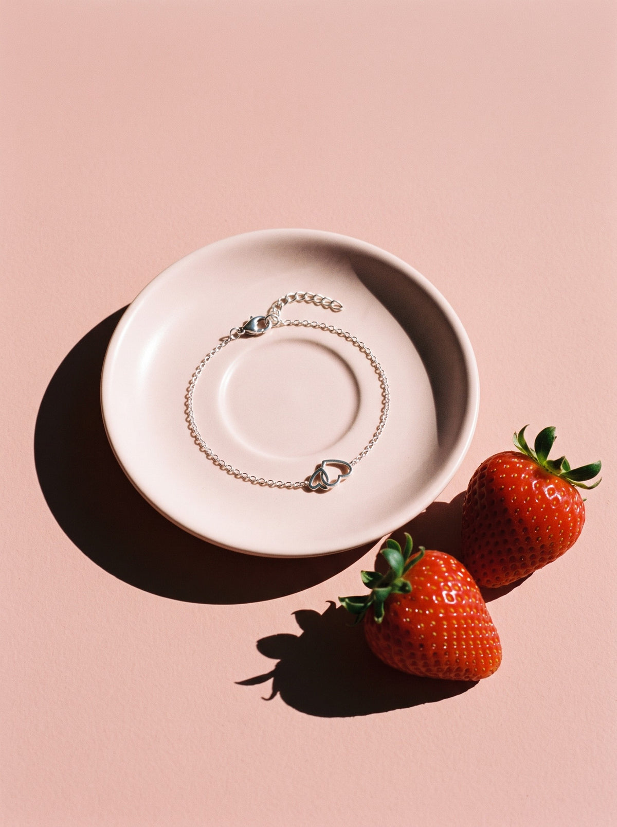 Lundholm Lieve armband met verbonden hartjes zilverkleurig op een roze schoteltje naast aardbeien