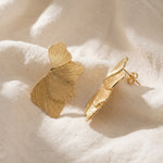 Detail Lundholm Linden ginkgo oorbellen goudkleurig op linnen, met stekersluiting zichtbaar