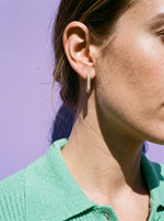 Vrouw in mintgroen vest draagt de Lundholm Loisa vierkante oorringen met zirkonia goudkleurig