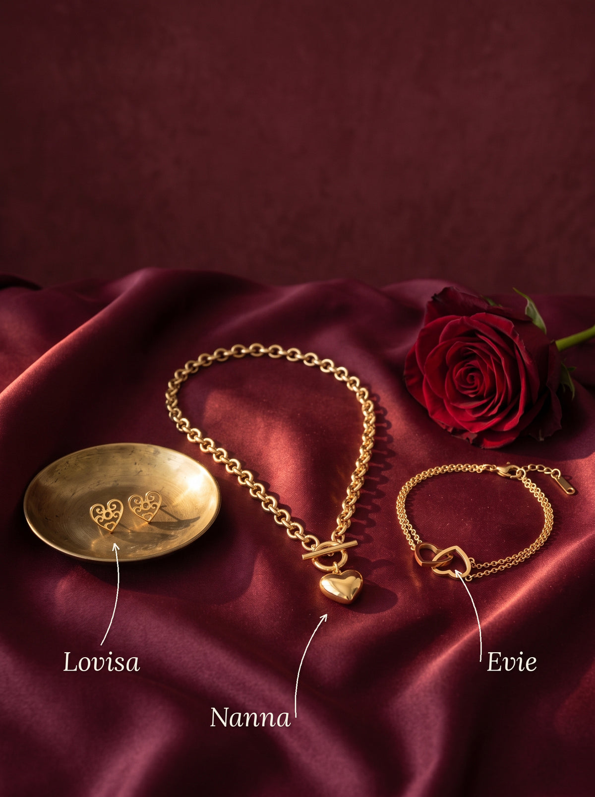 Lundholm Lovisa open hart oorknopjes, Nanna hartjes ketting met toggle sluiting en Evie armband met twee verbonden hartjes goudkleurig op bordeaux satijn met een rode roos