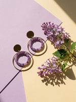 Lundholm Lucienne statement oorhangers met lila ring goudkleurig tussen paarse seringen