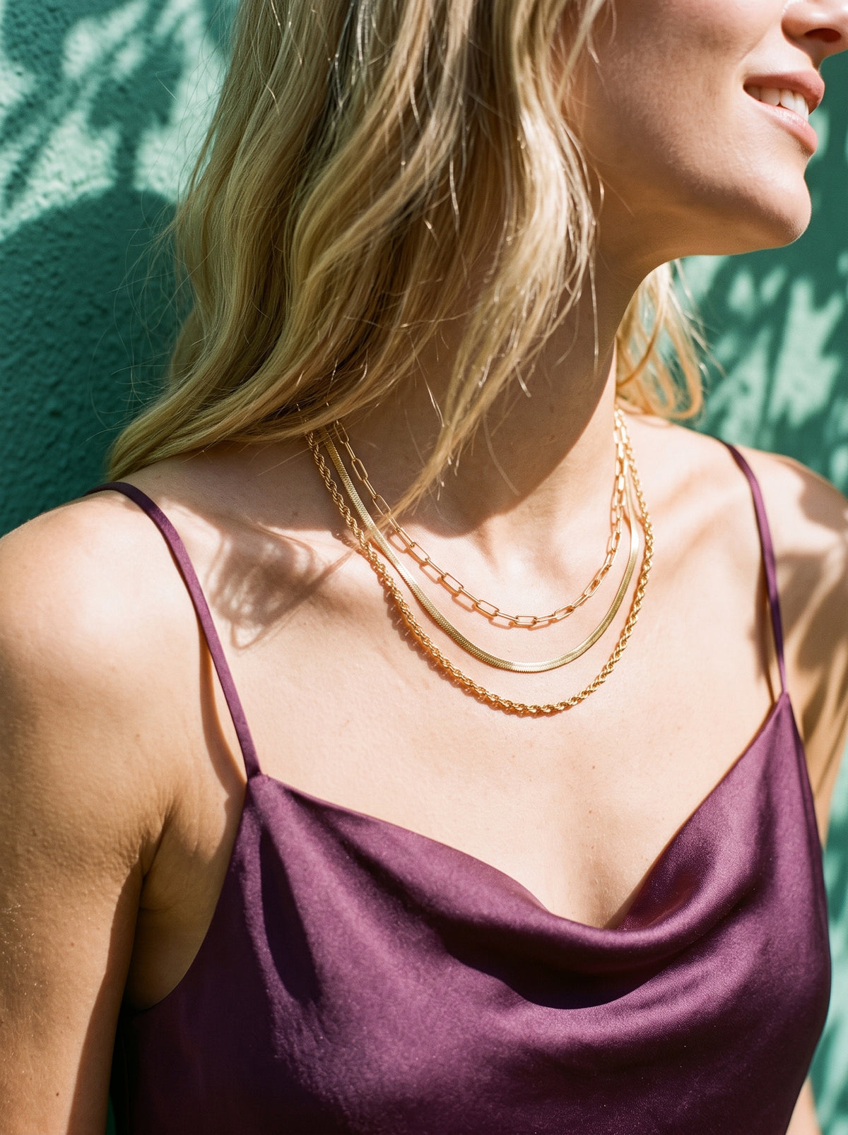 Vrouw draagt de Lundholm Manou drielaagse layered ketting goudkleurig op een pruimkleurige satijnen top