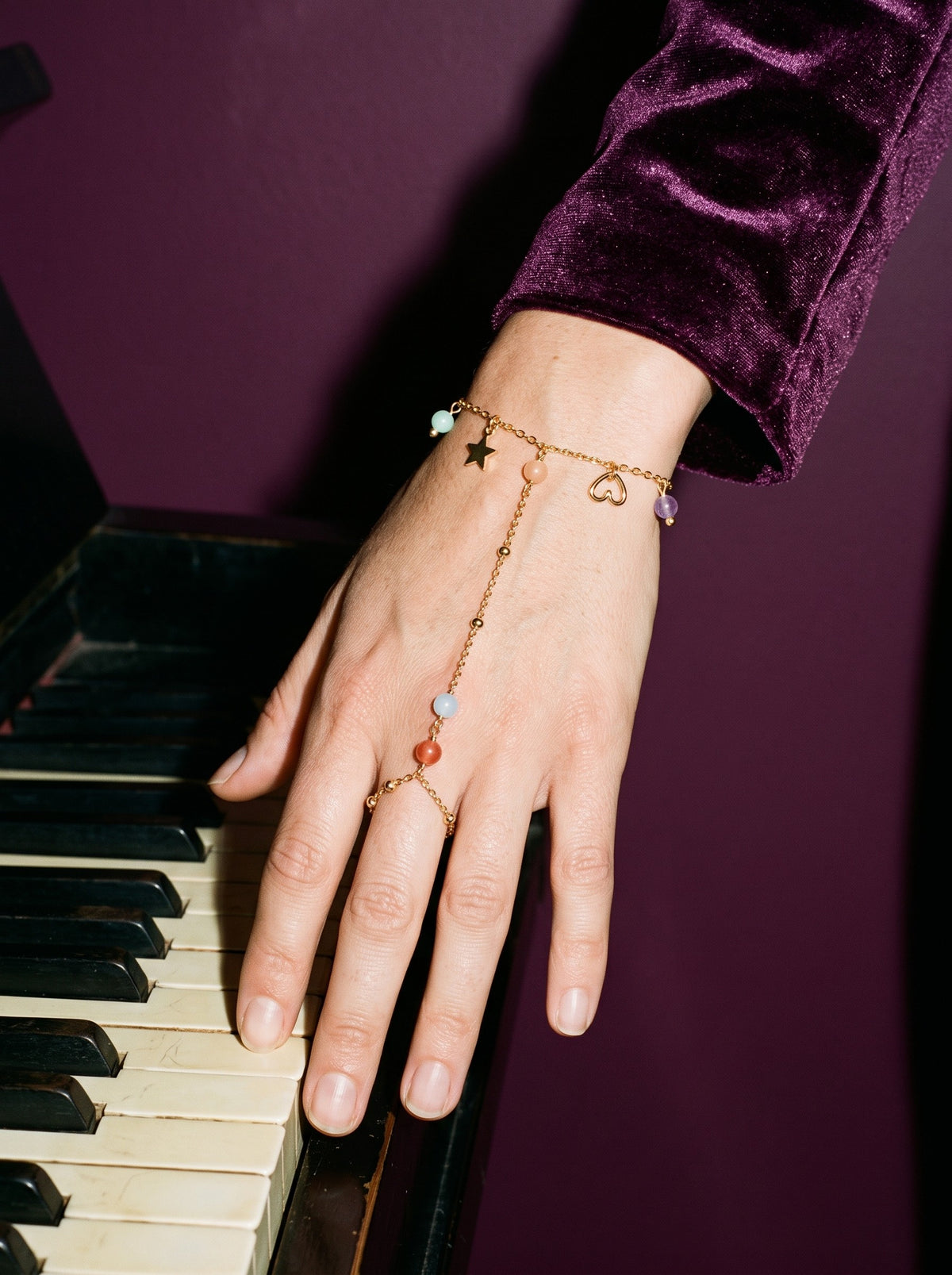 Lundholm Mona handsieraad met ring en bedels goudkleurig gedragen, hand op pianotoetsen