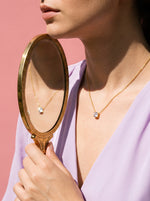 Vrouw draagt de Lundholm Monique ketting met zirkonia hanger goudkleurig, met een vintage handspiegel