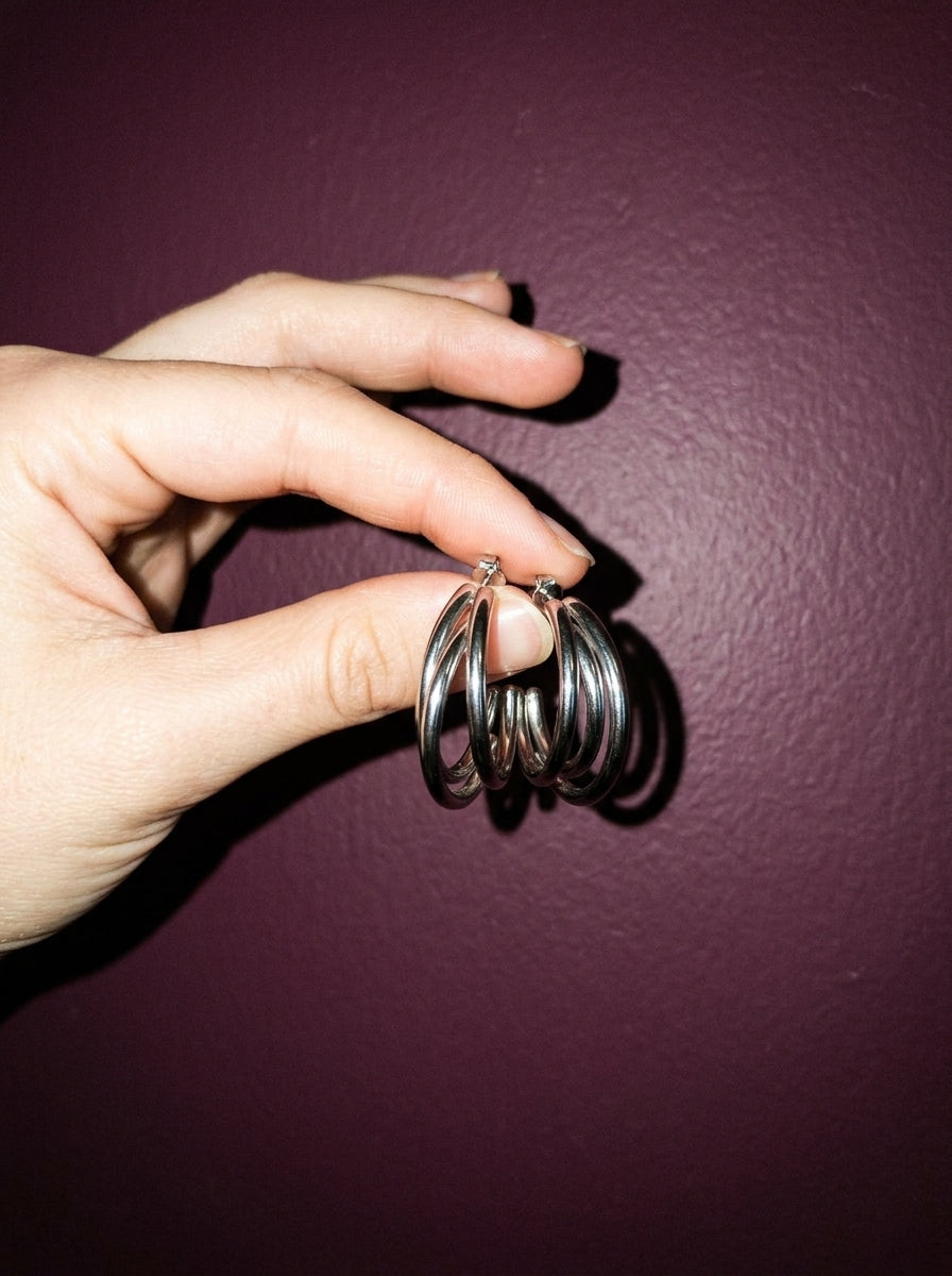Hand met de Lundholm Nika triple hoop oorbellen zilverkleurig voor een pruimkleurige muur