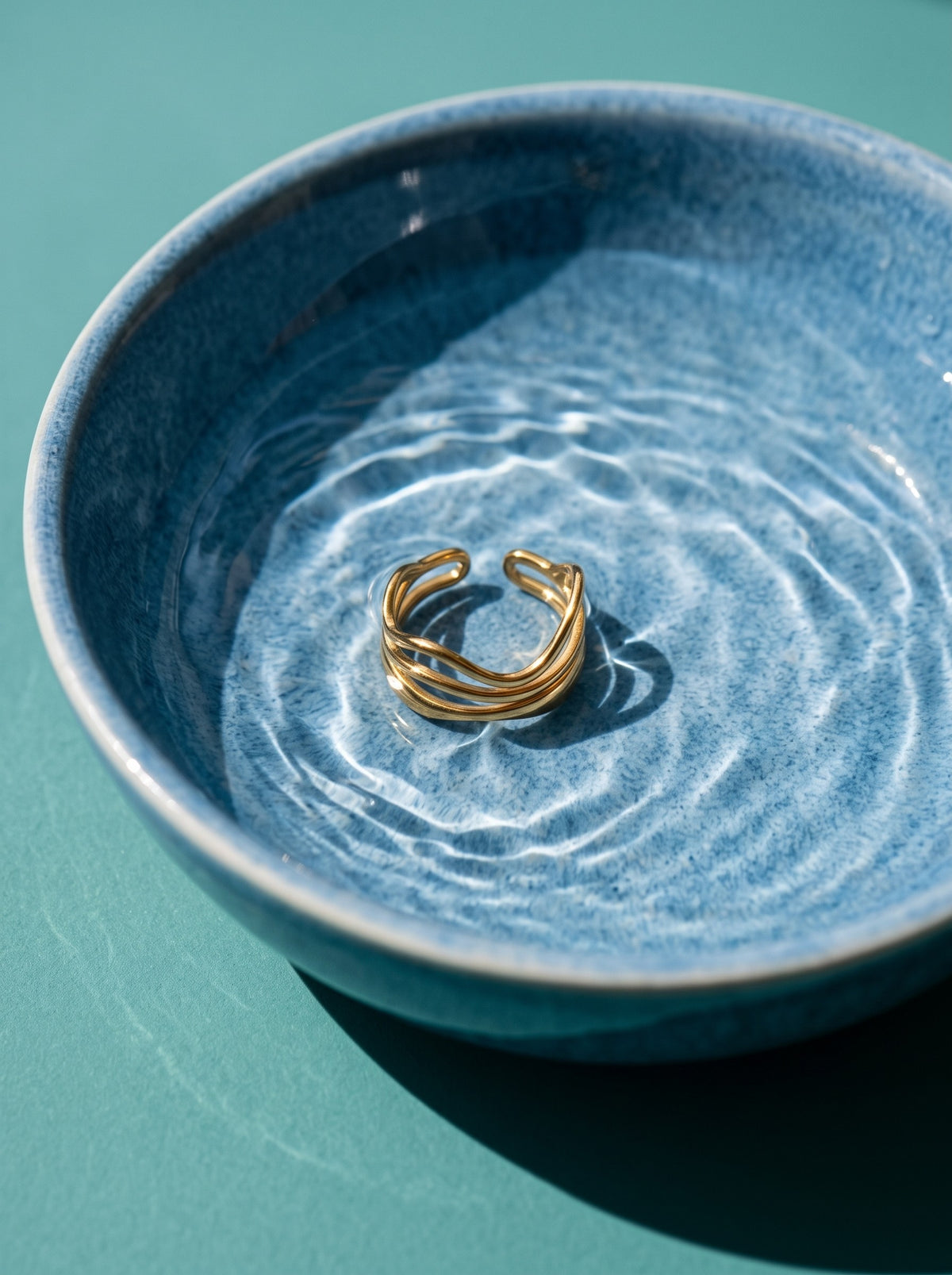 Lundholm Phoenix verstelbare gelaagde golfring goudkleurig in een blauwe schaal met water