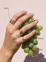Hand met de Lundholm Luce ring met zirkonia, Waves golfring en Elia golvende ring goudkleurig en een tros witte druiven