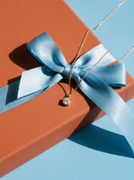 Lundholm Rosalie ketting met zirkonia hanger goudkleurig over een cadeaudoos met lichtblauw lint