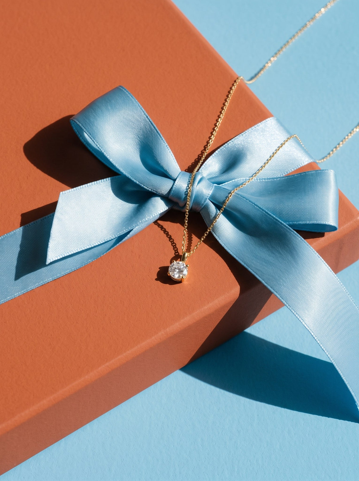 Lundholm Rosalie ketting met zirkonia hanger goudkleurig over een cadeaudoos met lichtblauw lint