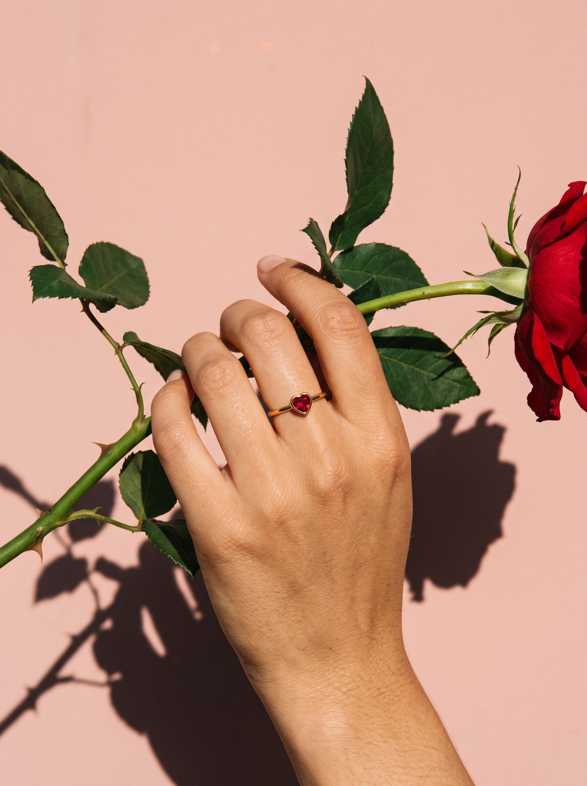 Lundholm Rose minimalistische ring met rood hartje goudkleurig gedragen, hand met een rode roos