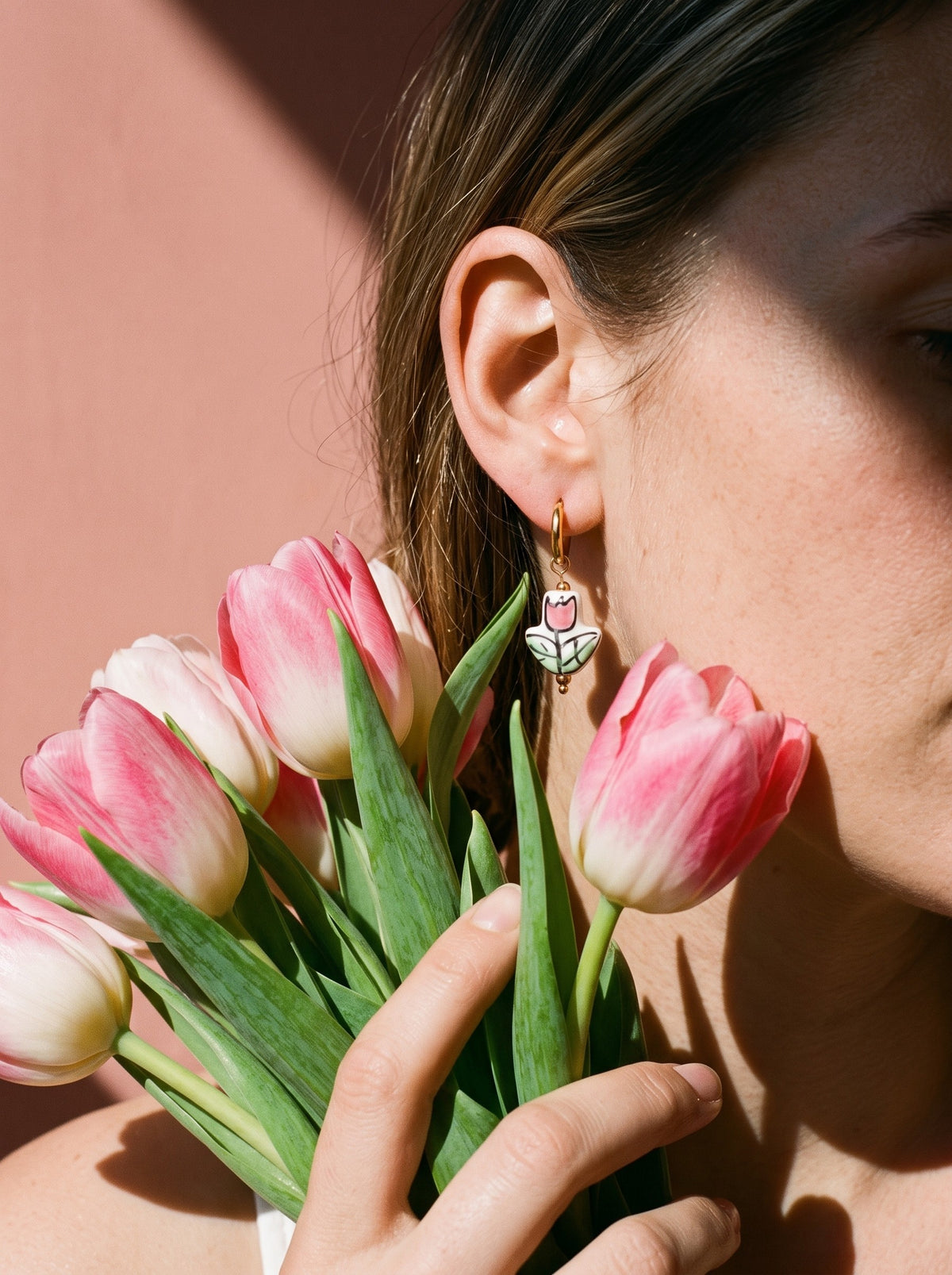 Vrouw draagt de Lundholm Saartje huggie oorringen met tulpen goudkleurig, met een bos roze tulpen