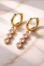 Lundholm Sam creolen oorbellen met roze zirkonia steentjes hangers in goudkleurig op marmer, sfeervolle styling
