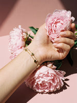 Lundholm Seya armband met hartjes en rozenkwarts goudkleurig gedragen, hand met roze pioenrozen
