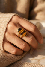 Lundholm Sienna verstelbare statement ring met grote tijgeroog steen in goudkleurig, gedragen aan vrouwenhand
