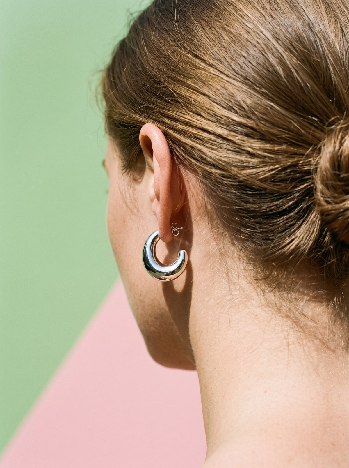 Vrouw met opgestoken haar draagt de Lundholm Simone chunky halve maan oorringen zilverkleurig