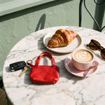 Rood sleuteletui met sleutels op een marmeren cafetafel naast cappuccino en croissant
