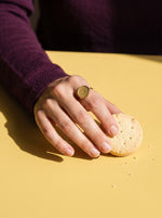 Lundholm Tamsin statement ring met ronde platte steen goudkleurig gedragen, hand met een zandkoekje