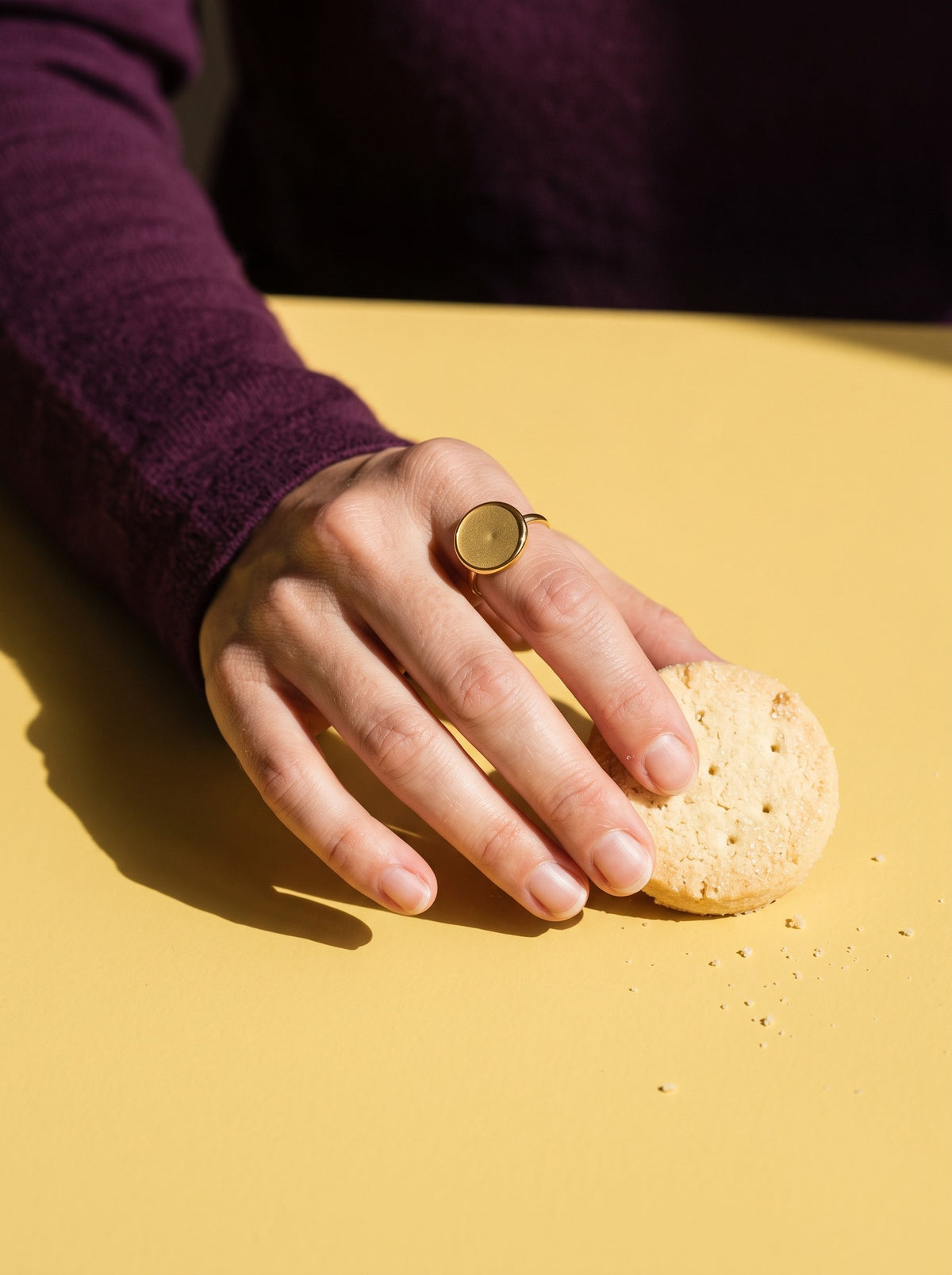 Lundholm Tamsin statement ring met ronde platte steen goudkleurig gedragen, hand met een zandkoekje