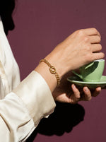Lundholm Tilda armband met verbonden ringen goudkleurig gedragen, hand met espressokopje