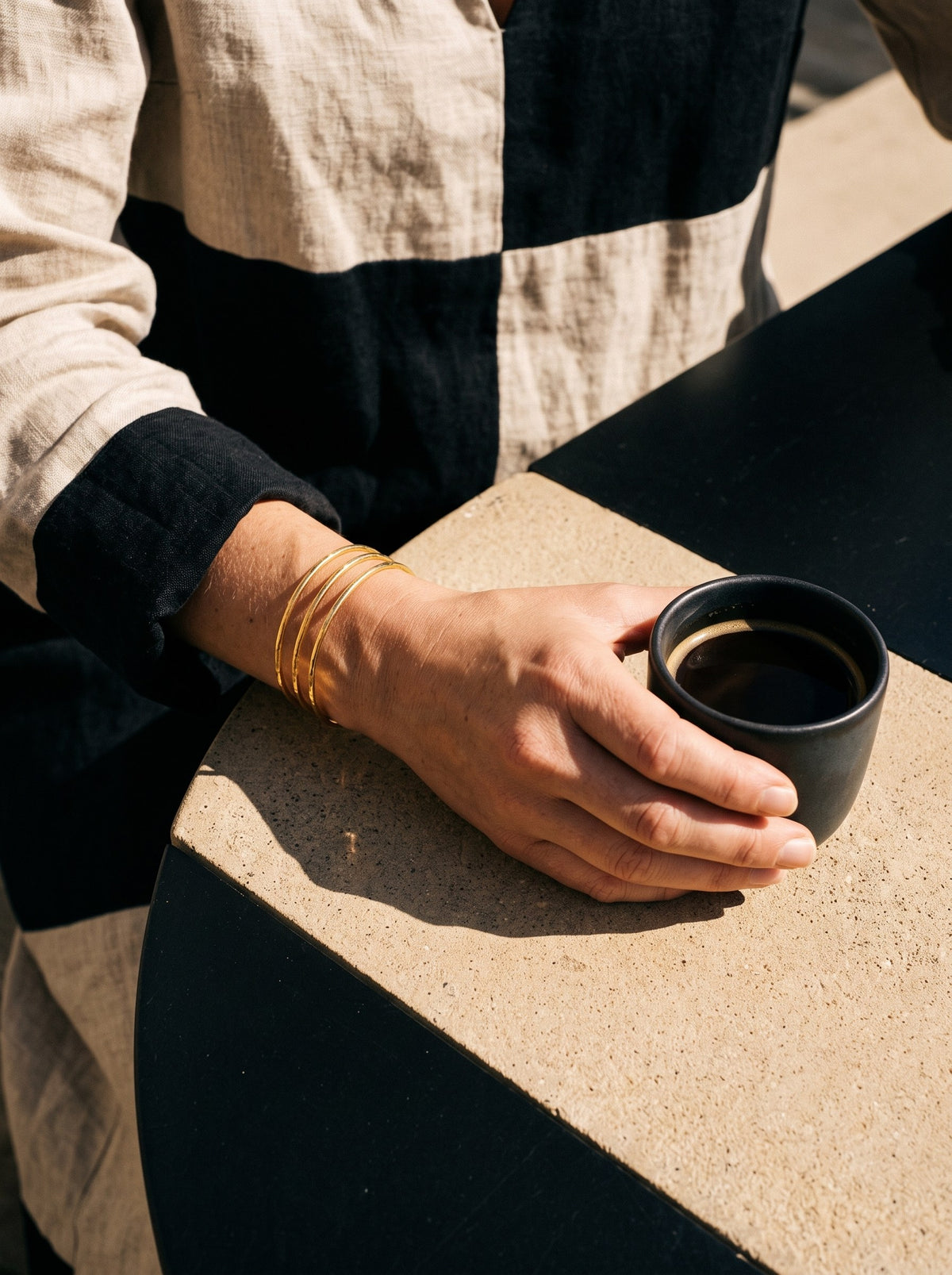 Lundholm Tindra open bangle met drie banen goudkleurig gedragen, hand om een espressokopje