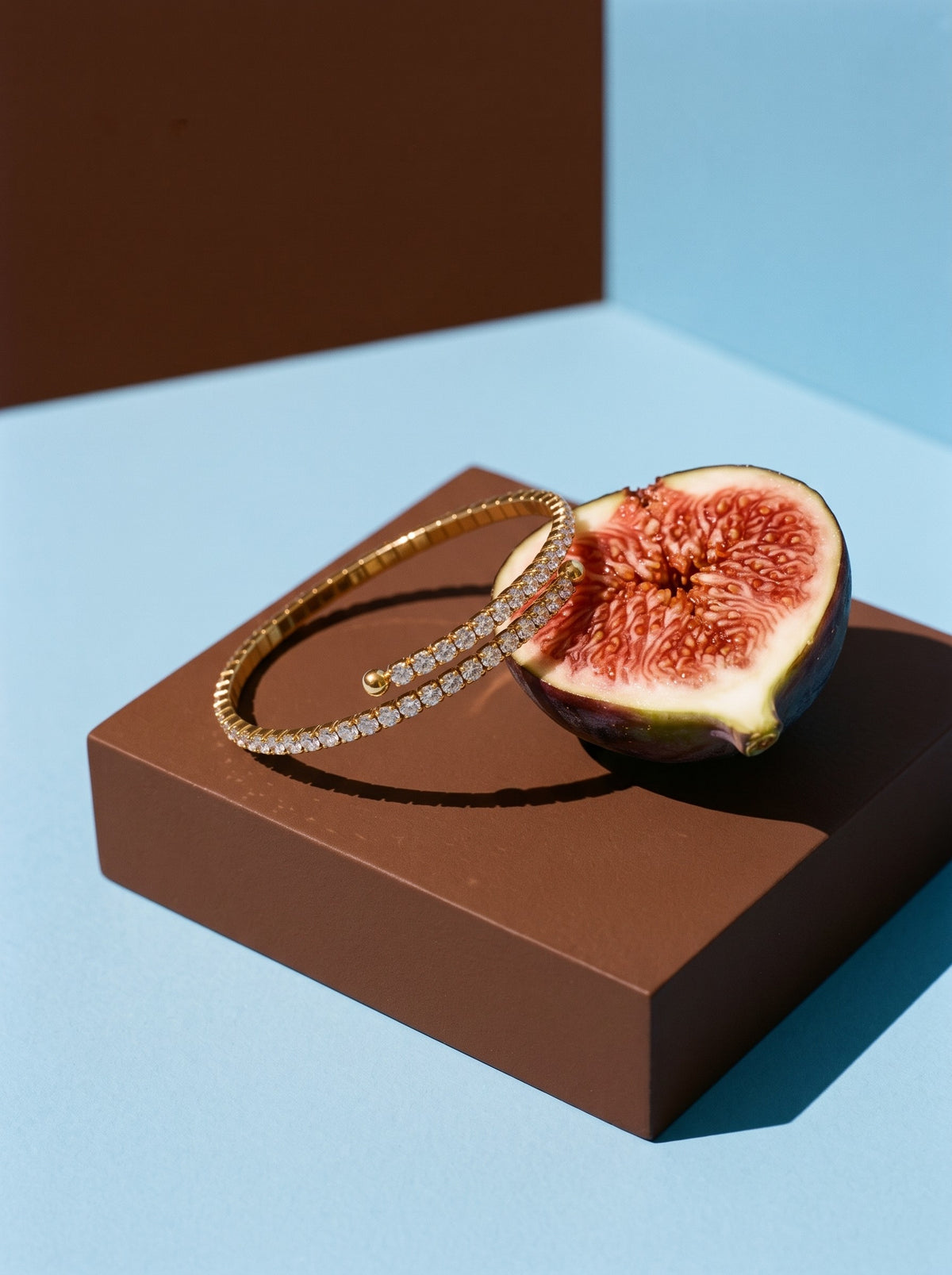 Lundholm Yael zirkonia tennisarmband bangle goudkleurig op een bruin doosje naast een halve vijg